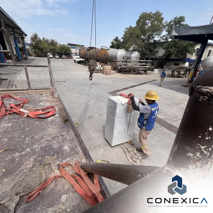 Personal de obra colocando un equipo con eslingas en una nave industrial