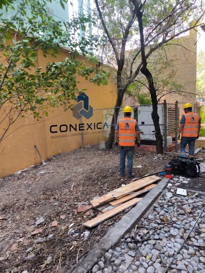 Dos trabajadores con chaleco naranja revisando un área de jardín antes de intervenirla